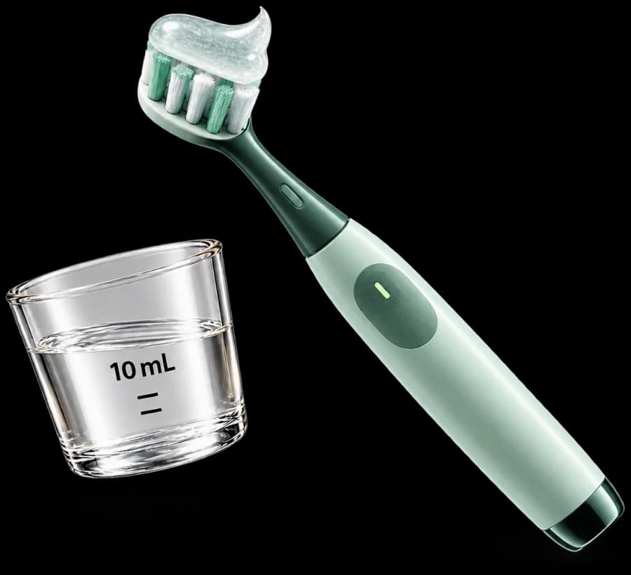 An electric toothbrush with gel across the bristles beside a clear 10 mL rinse cup